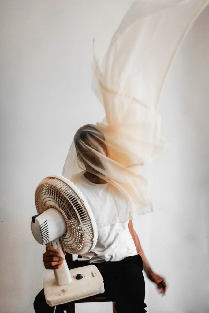 Abstract portrait of a person with a fan and flowing fabric, capturing motion indoors.